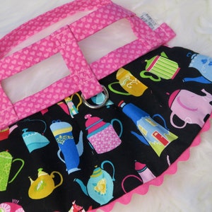 May include: Pink dog harness with a black fabric skirt featuring a teacup pattern. The skirt has a pink scalloped edge.