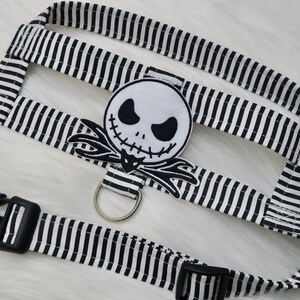 May include: Black and white striped dog harness with a black and white Jack Skellington character patch. The harness has two black plastic buckles and a silver metal D-ring.