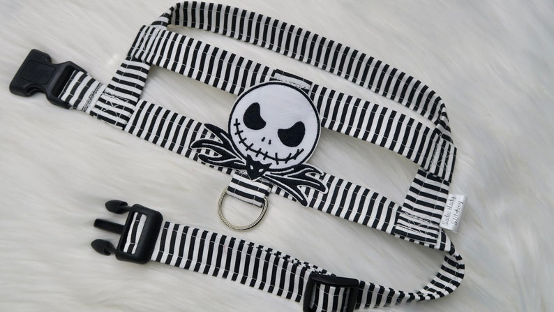 May include: Black and white striped dog harness with a black and white Jack Skellington character patch. The harness has two black plastic buckles and a silver metal D-ring.
