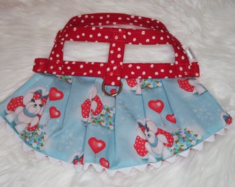 May include: A blue and white dog-themed harness with a red polka dot top. The harness has a white ruffle trim and a red polka dot strap.