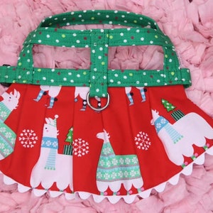 May include: A red and white dog harness with a green and white polka dot strap. The harness features a festive llama print with snowflakes and Christmas trees.