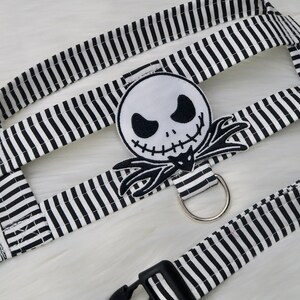 May include: Black and white striped dog harness with a black and white Jack Skellington character patch. The harness has a black plastic buckle and a silver metal ring.