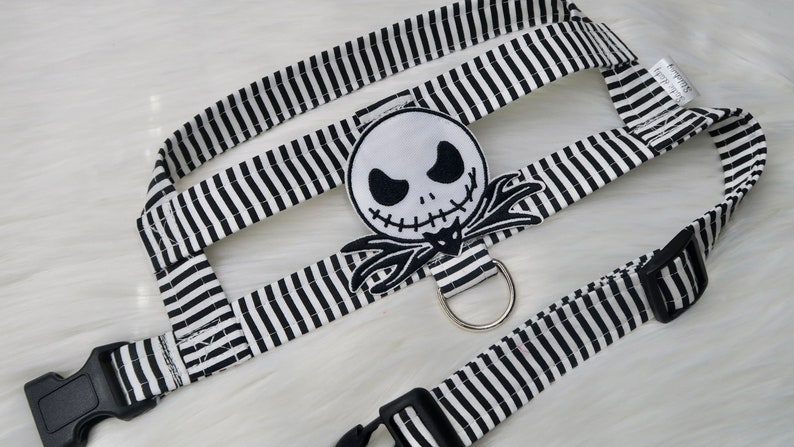 May include: Black and white striped dog harness with a black and white Jack Skellington character patch. The harness has a black plastic buckle and a silver metal ring.