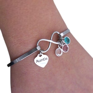 May include: A silver infinity charm bracelet with a heart charm that says "Auntie" and three small round charms with colorful gemstones.