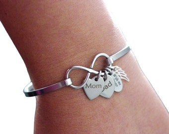 May include: A silver-toned bracelet featuring an infinity symbol and heart-shaped charms. The charms are engraved with the words "Mom" and "Dad", and a charm with angel wings and the words "With me always".