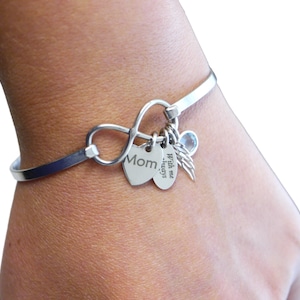 May include: Silver infinity charm bracelet with a heart charm that says "Mom" and a charm that says "With me always" with a small angel wing charm and a light blue crystal charm.