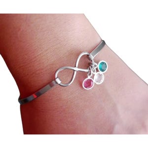 May include: A silver infinity charm bracelet with three dangling charms. The charms are pink, white, and green.