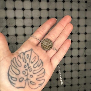 May include: A silver chain necklace with a round pendant featuring a brown and white patterned design.