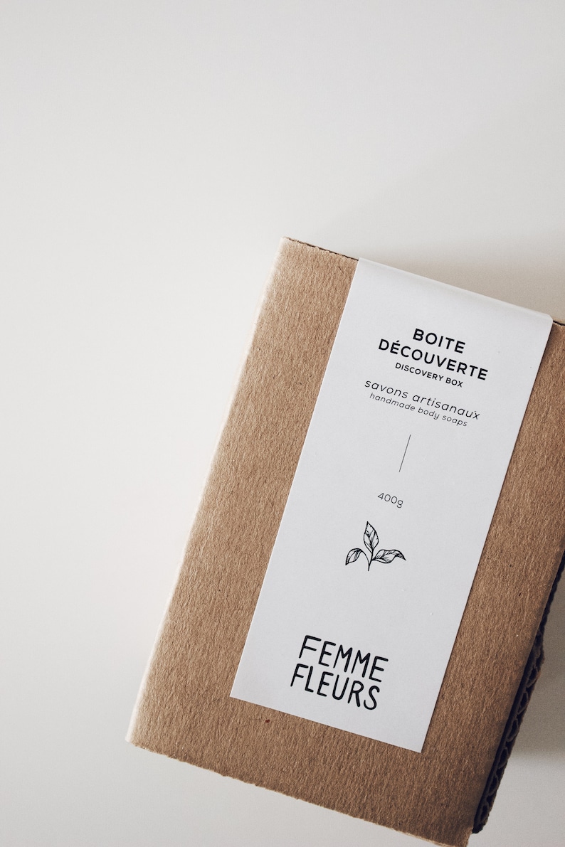 Puede incluir: Una caja rectangular de cart&oacute;n marr&oacute;n con una etiqueta blanca. La etiqueta dice "BOITE D&Eacute;COUVERTE DISCOVERY BOX savons artisanaux handmade body soaps" y "FEMME FLEURS". La caja contiene 400g de producto y una ilustraci&oacute;n de hoja.