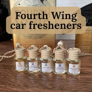May include: Five glass car freshener bottles with wooden caps and hanging cords. Each bottle has a label with a different name: "Fourth Wing", "Flying With Tairn", "The Vale", "Xaden's Shadows", and "Andarna's Magic". The text "Fourth Wing car fresheners" is displayed above the bottles.