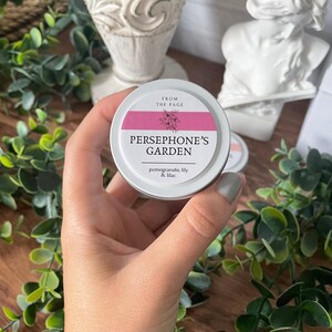 May include: A small, silver tin with a pink label that reads "From the Page, Persephone's Garden, pomegranate, lily & lilac".