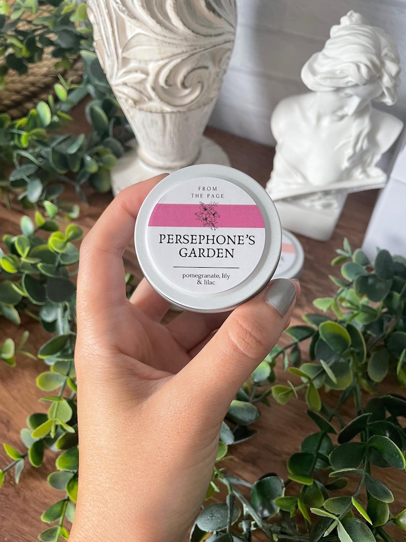 May include: A small, silver tin with a pink label that reads "From the Page, Persephone's Garden, pomegranate, lily & lilac".