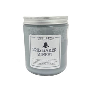 May include: A gray soy candle in a glass jar with a silver lid. The label reads "221B BAKER STREET" with the text "black tea & leather books." The candle is hand poured and vegan, and is 8 oz.