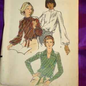May include: Vintage Vogue Patterns sewing pattern. The package features illustrations of three blouses. The top left blouse is striped with red, orange, and green. The top right blouse is white with long sleeves. The bottom blouse is green with a diamond pattern. The package reads "Vogue Patterns".