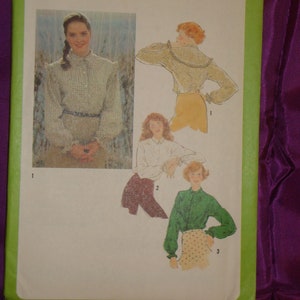 May include: A vintage Simplicity sewing pattern, size 14 Miss, featuring illustrations of blouses. The pattern envelope is green with the Simplicity logo and the number 9117. The image includes a photo of a woman wearing a blouse.