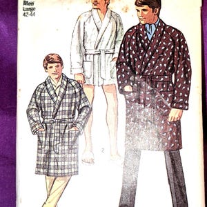 May include: A Simplicity 8470 sewing pattern envelope for a robe in size Large 42-44. The illustration shows three variations of a robe: one in a plaid pattern, one in a solid light color, and one in a dark color with a white paisley print.