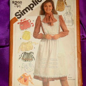 May include: Simplicity sewing pattern 5323 featuring apron designs. The package shows a woman wearing an apron with a white bib and a brown blouse. The package includes illustrations of various apron styles, with the text "View 3: Patterns for appliqués included."