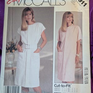 May include: An Easy McCall's 2911 sewing pattern envelope featuring a white dress with a belt and pockets, and a light pink dress with short sleeves and pockets. The text includes Easy McCall's 2911, Woman's Day Collection, and Cut-to-Fit.