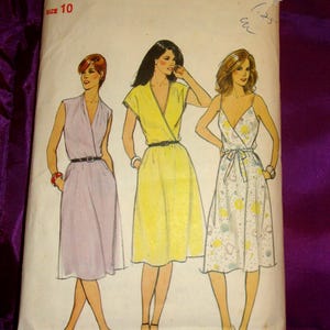 May include: Vintage Butterick sewing pattern featuring illustrations of three wrap dresses. The dresses are in shades of lavender, yellow, and white with floral accents. The pattern is size 10.