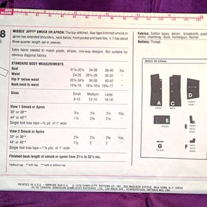 May include: A white Simplicity sewing pattern envelope for a Jiffy smock or apron, model 7708, featuring 7 pieces. The back of the envelope displays technical illustrations, fabric requirements, and standard body measurements in inches for sizes small to large.