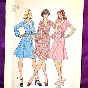 May include: Simplicity sewing pattern 6788 featuring three wrap dresses. The pattern includes a size 12 with a 34-inch bust. The dresses are in blue with white polka dots, floral print, and solid pink. The pattern is for Misses.