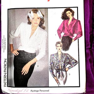 May include: A sewing pattern envelope titled Personalized Fit Ajustage Personnel featuring illustrations of three wrap-style blouses. One blouse is solid white, one is solid magenta, and one features a floral pattern with long sleeves and a front tie.