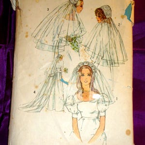 May include: A vintage Simplicity 826 sewing pattern envelope featuring illustrations of four different bridal veil styles. The paper envelope is off-white with brown age spots and displays numbered sketches of veils with floral headpieces.