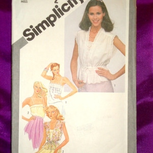 May include: A vintage Simplicity sewing pattern package featuring illustrations of women's clothing designs. The package includes a photo of a woman wearing a white top and illustrations of other outfits. The text on the package reads "Simplicity" and "9971".