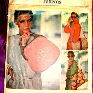 May include: A Vogue Patterns sewing envelope labeled 1406 featuring illustrations of three different handbag styles. One bag is pink with monogrammed letters, another is a neutral tone with a striped strap, and the third features a floral print pattern.