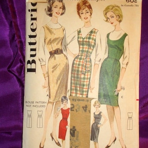 May include: Vintage Butterick sewing pattern envelope featuring illustrations of three dresses. The envelope is cream-colored with text and illustrations in black, red, and green. The bust size is 34, and the size is 14. The pattern is for a "proportioned jumper".
