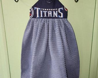 May include: A blue kitchen towel with a Tennessee Titans logo on the hanging loop. The towel is hanging on a wooden rod.
