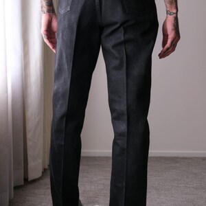 Peut inclure: Jean noir en denim avec une conception classique &agrave; cinq poches. Le jean a une coupe droite et comporte un patch en cuir marron sur la poche arri&egrave;re. Le jean est port&eacute; avec un d&eacute;bardeur blanc.
