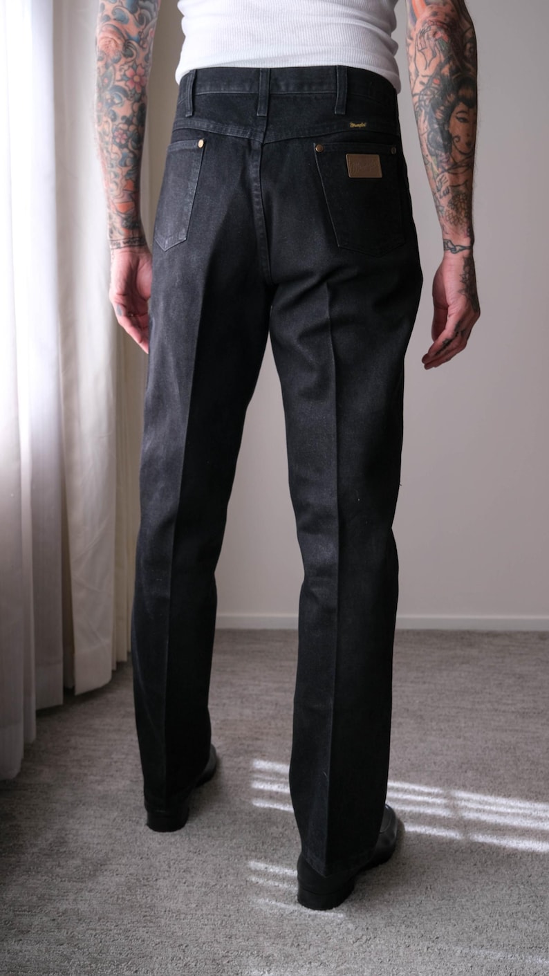 Peut inclure: Jean noir en denim avec une conception classique &agrave; cinq poches. Le jean a une coupe droite et comporte un patch en cuir marron sur la poche arri&egrave;re. Le jean est port&eacute; avec un d&eacute;bardeur blanc.