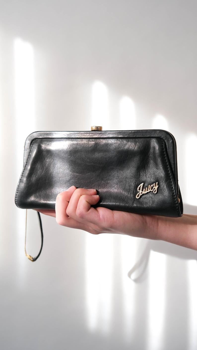 May include: A black leather clutch purse with a gold clasp and the word "Juicy" in gold lettering.