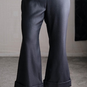 May include: Dark gray flared pants with a cuffed hem. The pants are paired with black high-heeled sandals with decorative straps. The fabric has a subtle texture. The pants are a classic style.