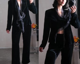 May include: A black velvet suit with a matching jacket and pants. The jacket has a shawl collar and a draped scarf detail. The pants have a wide leg.