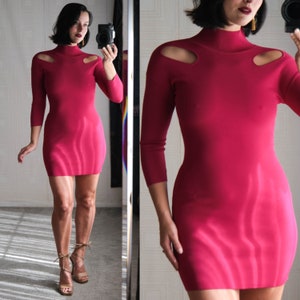 May include: A bright pink, form-fitting dress with a high neck and cut-out shoulders. The dress has long sleeves and a mini length.