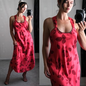 May include: A red halter dress with a dark leaf pattern. The dress has a black trim around the neckline and straps. The dress is a midi length.