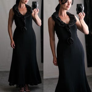 Puede incluir: Un vestido negro de maxi sin mangas con un escote de volantes y un gran adorno de flor negra en la cintura.