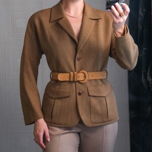May include: A brown blazer with a matching belt and tan pants. The blazer has two front pockets and a classic collar. The belt cinches the waist. The outfit is a neutral color palette, suitable for a professional or smart casual look.