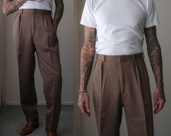 May include: A pair of brown trousers featuring a high-waisted design with double pleats at the front, a structured waistband with belt loops, and a straight-leg cut. The trousers are paired with a plain white short-sleeved crew neck t-shirt.
