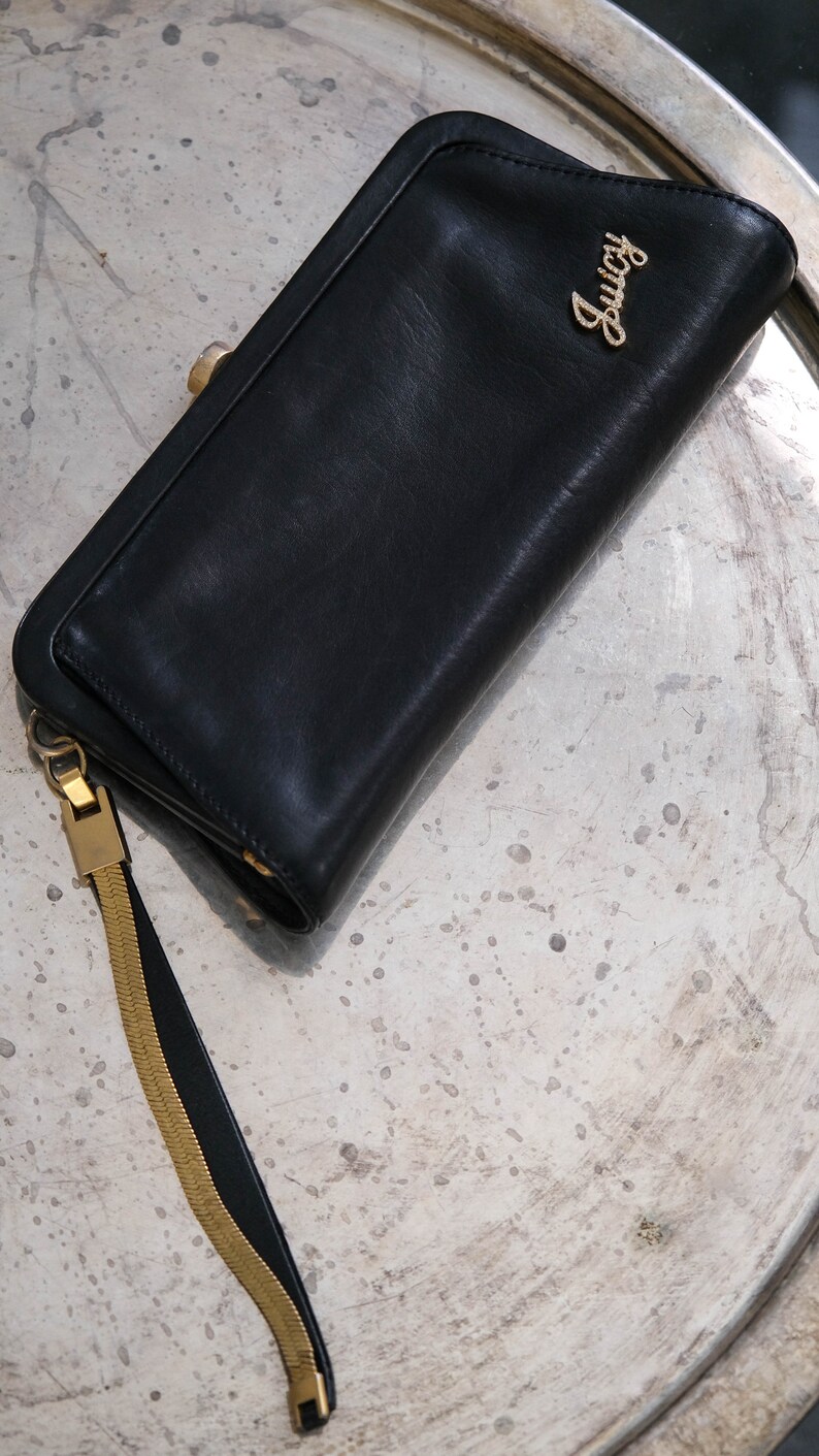 May include: A black leather wallet with a gold chain strap and the word "Lucy" embossed in gold on the front.