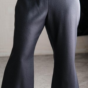 May include: Dark gray flared pants with a tailored fit. The pants have a high waist and a subtle texture. The cuffs are turned up at the hem. The pants are made of a woven fabric.