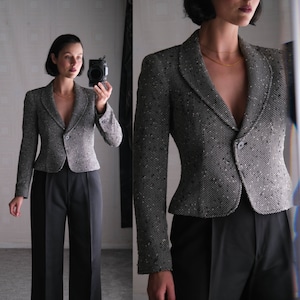 May include: A black and white tweed blazer with a single button closure and a pointed collar. The blazer is cropped and fitted.