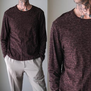 May include: A long-sleeved, crew neck shirt in a deep burgundy color with a subtle leopard print pattern. The shirt is paired with light beige trousers. The fabric appears soft and drapes well. The overall style is casual and comfortable.
