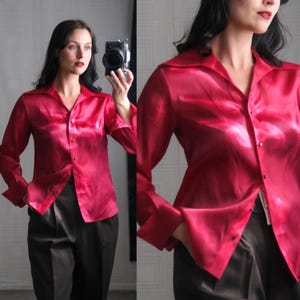 May include: A bright red, long-sleeved shirt with a button-down front. The shirt has a classic collar and cuffs, made from a silky, shiny material. It is worn with dark, tailored trousers.