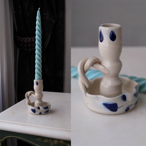 Pode incluir: Castiçal de cerâmica branco com um design floral azul e branco. O castiçal tem uma alça torcida e uma base larga.