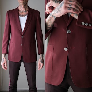 Könnte beinhalten: Ein weinrotes Sakko mit Zwei-Knopf-Verschluss und zwei Vordertaschen. Das Sakko hat ein fallendes Revers und eine taillierte Passform. Die Ärmel haben drei dekorative Knöpfe. Das Sakko wird mit weinroten Hosen kombiniert.