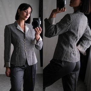 May include: A black and white patterned blazer with a fitted silhouette. The blazer has a notched collar, long sleeves, and a button closure. The model is wearing black pants.