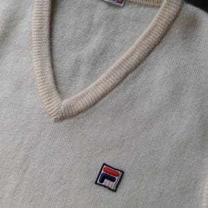 Peut inclure: Pull-over cr&egrave;me &agrave; col en V avec un petit &eacute;cusson FILA sur la poitrine. Le pull a une encolure c&ocirc;tel&eacute;e et une petite &eacute;tiquette FILA. Le pull est fait d'une mati&egrave;re tricot&eacute;e douce.